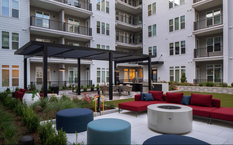 a fire pit with seating and grilling area in the background with a pergola 