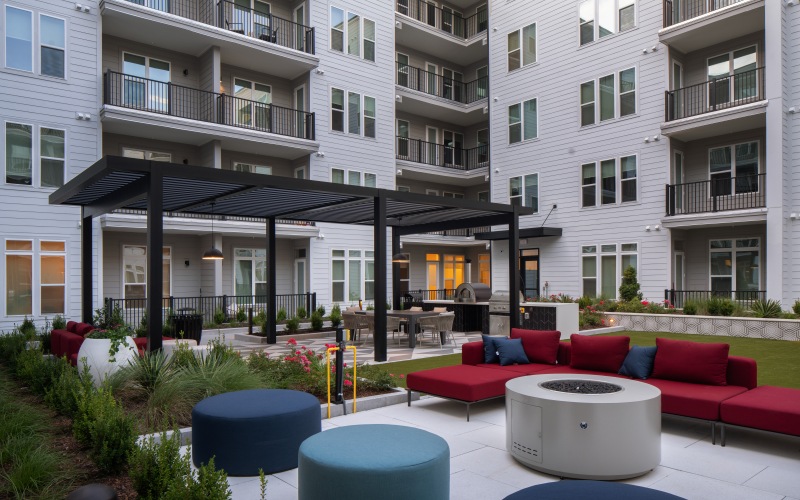 a firepit with seating and grilling area in the background with a pergola 